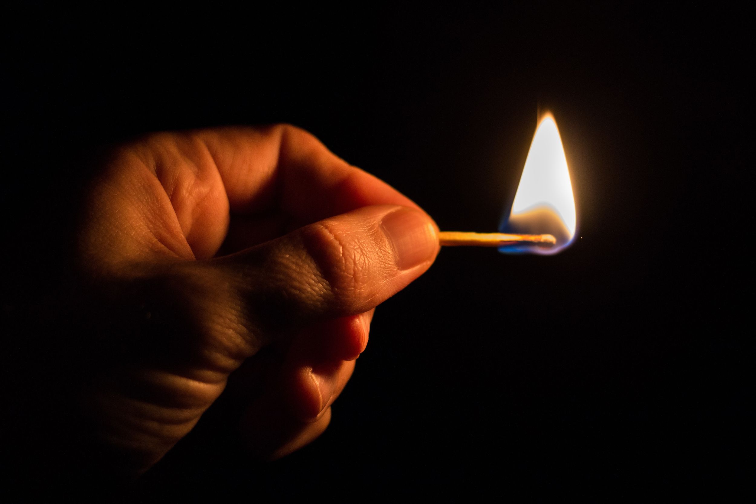 Close-up of a non-melanated hand holding a lit match in darkness